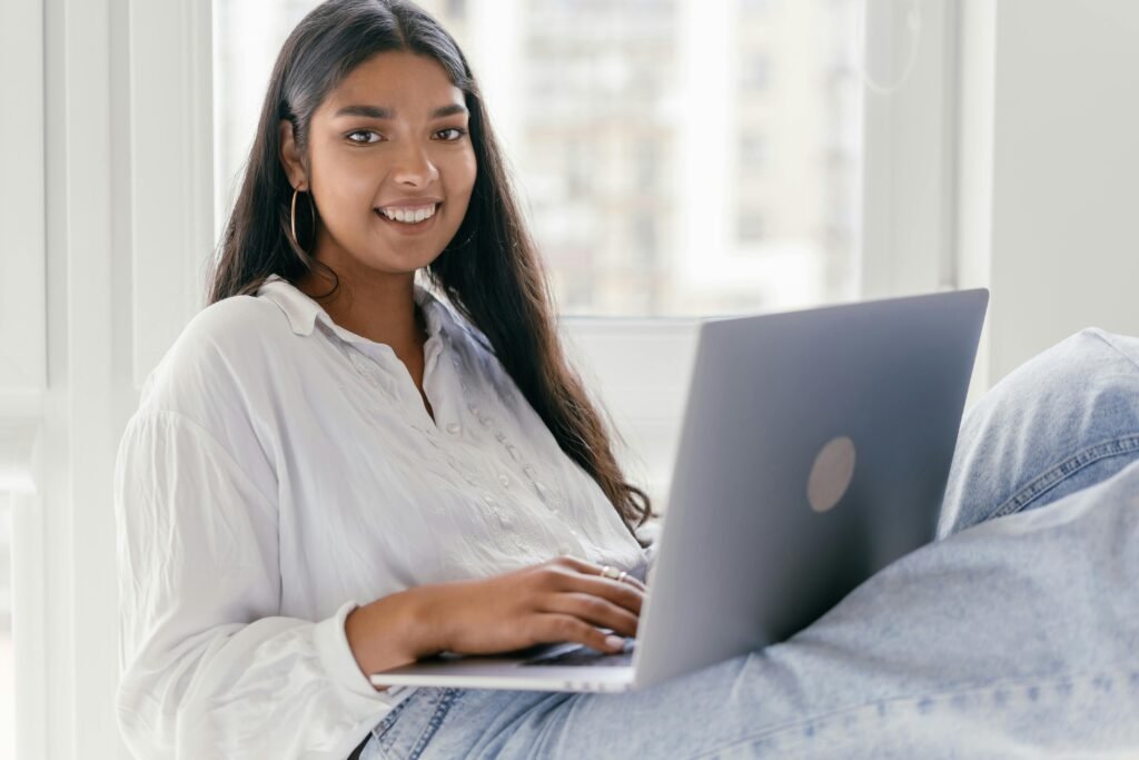 Woman relaxing and working from home on her laptop near a bright window.