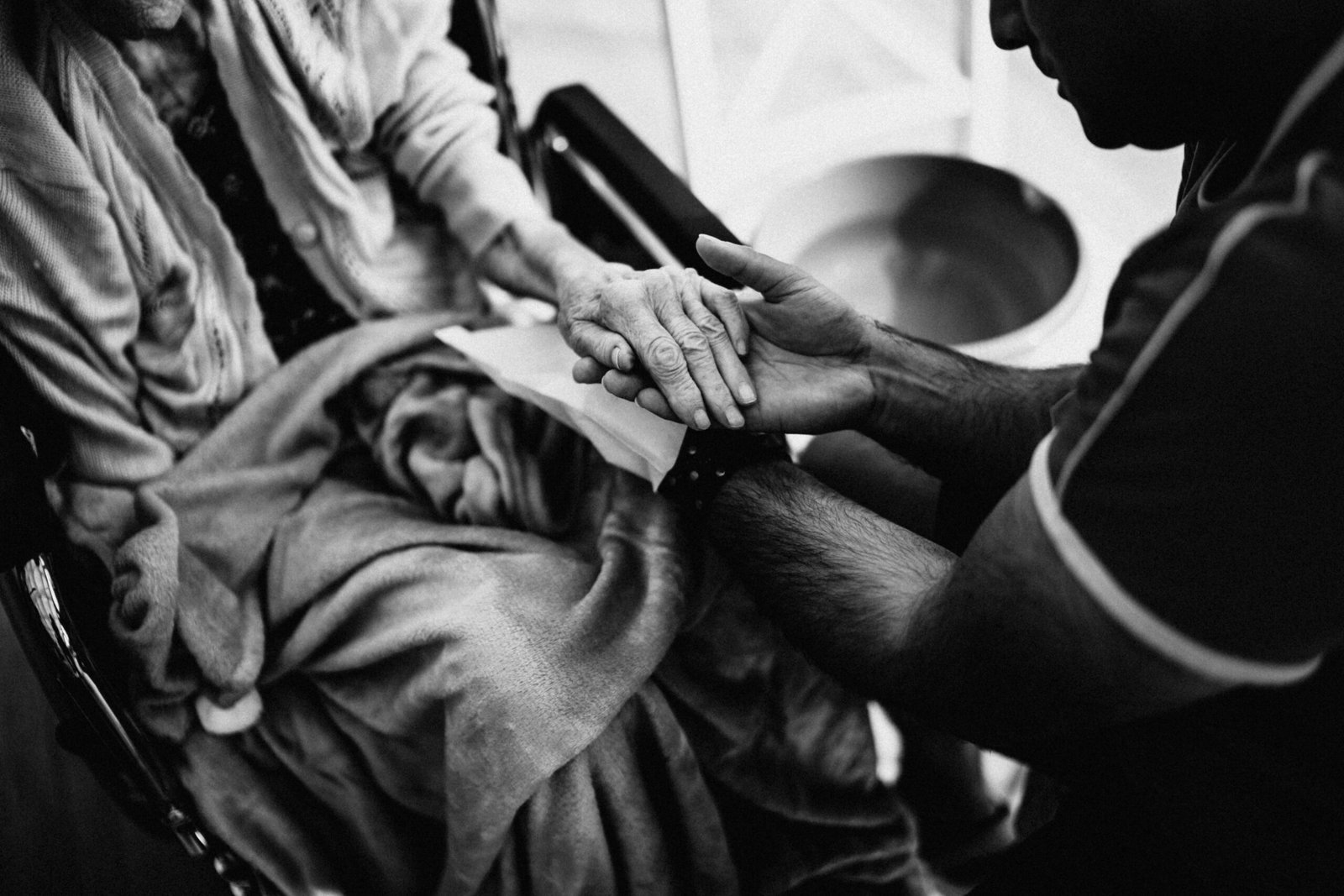 A caregiver holding the hands of an elderly woman in a wheelchair, emphasizing empathy and support.